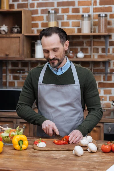 Счастливый человек нарезает перец на кухне — стоковое фото