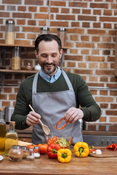 Lächelnder Mann, der Paprika zum Salat hinzufügt — Stockfoto