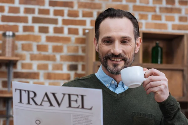 Bell'uomo che tiene una tazza di caffè e legge un giornale di viaggio — Foto stock