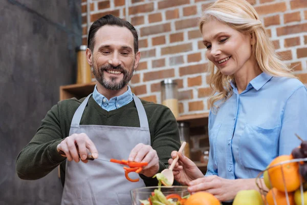 Happy affectionate couple preparing salad in kitchen — Stock Photo
