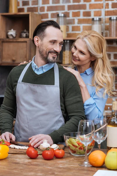 Femme étreignant mari alors qu'il cuisine à la cuisine — Photo de stock