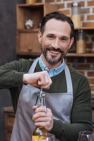 Hombre sonriente abriendo botella de vino con sacacorchos y mirando a la cámara - foto de stock