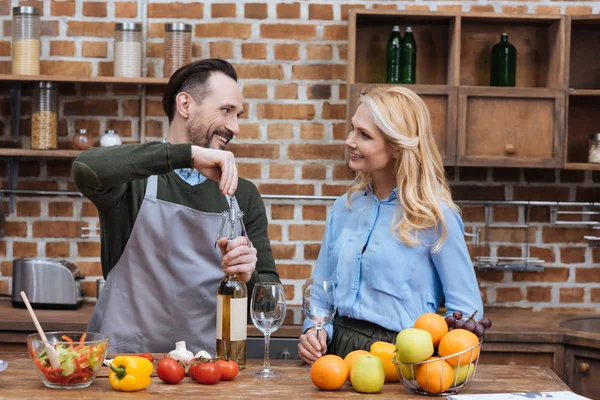 Sonriente marido abriendo botella de vino con sacacorchos y mirando a la esposa - foto de stock