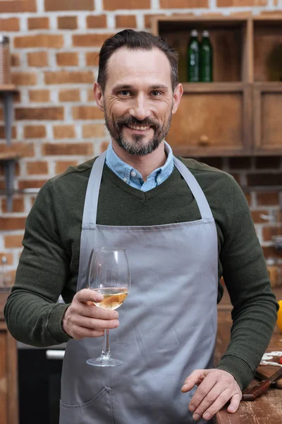 Lächelnder Mann mit einem Glas Wein und Blick in die Kamera in der Küche — Stockfoto