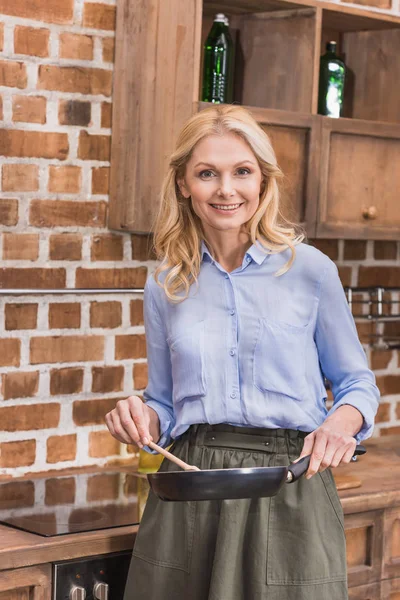 Attractive woman standing with frying pan and wooden spatula — Stock Photo