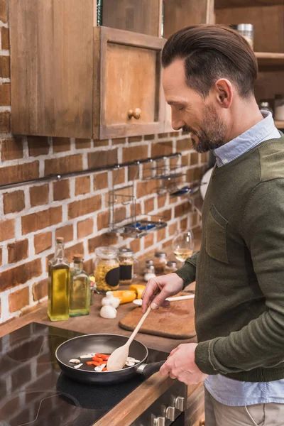 Schöner Mann rührt Gemüse in Pfanne — Stockfoto