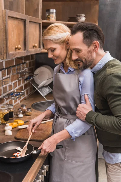 Ehemann umarmt Ehefrau, während sie in der Küche kocht — Stockfoto