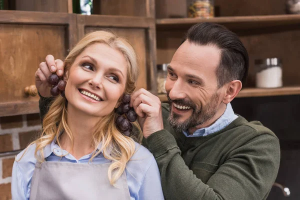 Husband making earrings to wife with grapes — Stock Photo