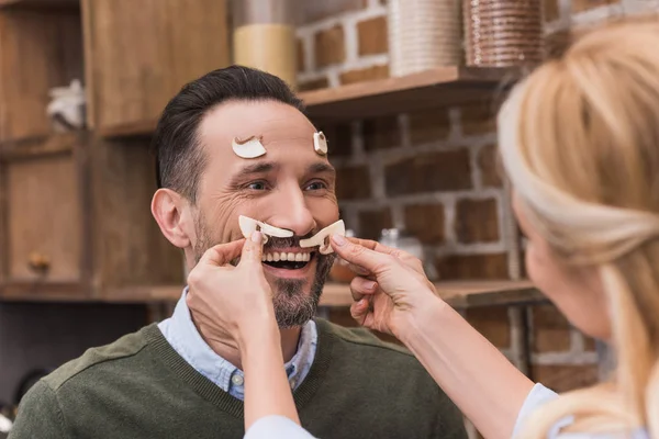 Wife putting pieces of mushrooms on husband face — Stock Photo