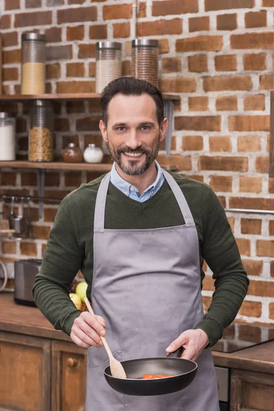 Hombre guapo con sartén y espátula de madera mirando a la cámara — Stock Photo