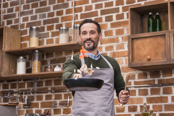 Handsome man tossing up vegetables on frying pan — Stock Photo