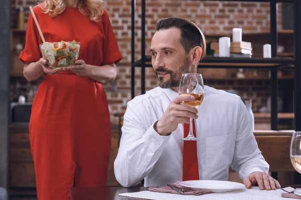 Image recadrée de femme servant table avec salade appétissante et mari buvant du vin au dîner romantique — Photo de stock