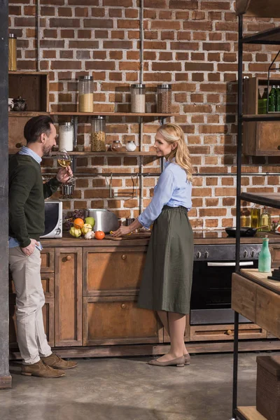 Husband drinking wine and wife cooking at kitchen — Stock Photo