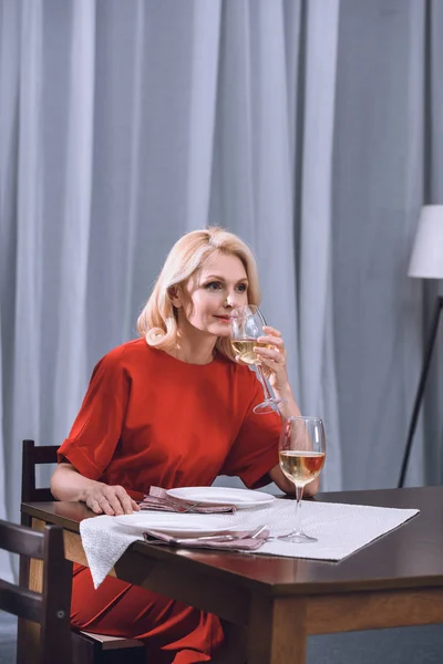 Schöne Frau in rotem Kleid trinkt Wein am Tisch — Stockfoto