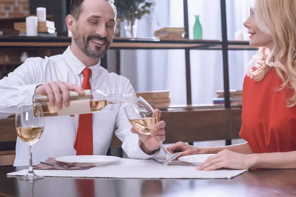 Муж наливает вино в бокал жены за романтическим ужином — стоковое фото