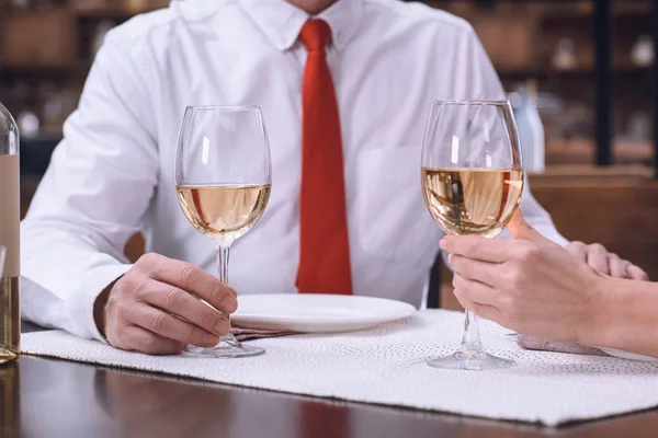 Cropped image of couple holding hands and glasses of white wine at romantic dinner — Stock Photo