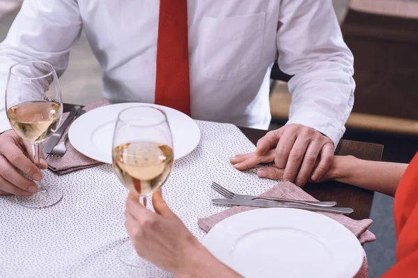 Cropped image of couple holding hands and glasses of wine at romantic date — Stock Photo