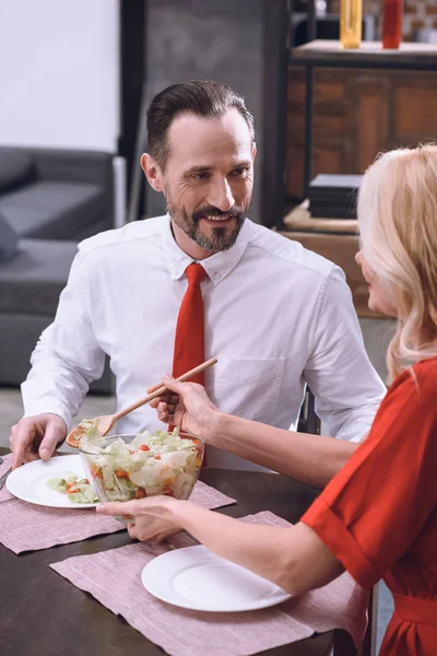 Wife putting salad on smiling husband plate at romantic date — Stock Photo