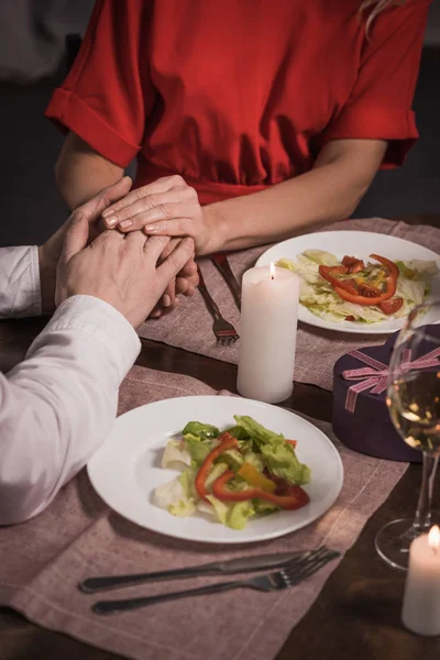 Image recadrée d'un couple tenant les mains et des assiettes avec salade sur la table — Photo de stock