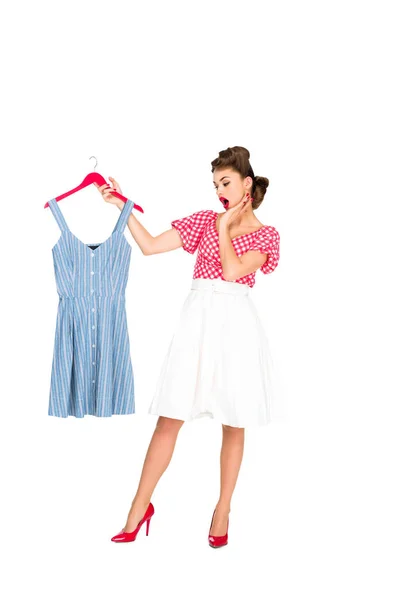 Impactado mujer con estilo en ropa retro mirando vestido en percha en la mano aislado en blanco - foto de stock