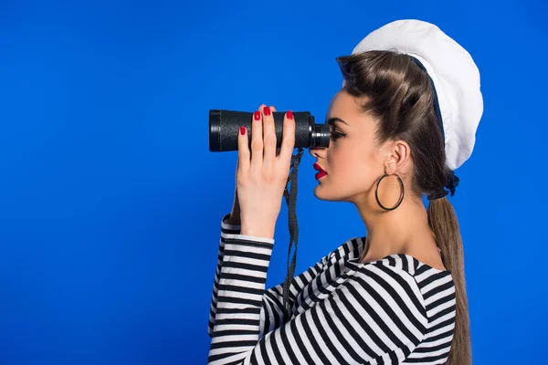 Vista laterale di attraente giovane donna in abiti retrò con binocolo isolato su blu — Foto stock