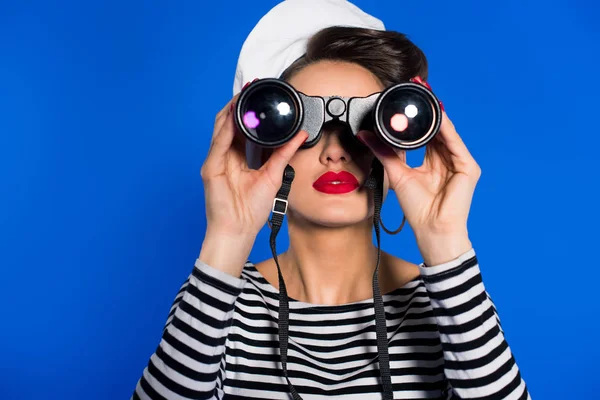 Vista oscurecida de la atractiva joven en ropa retro con prismáticos aislados en azul - foto de stock