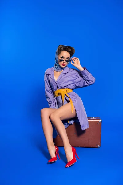 Mulher jovem na moda em roupas retro com mala isolada em azul — Fotografia de Stock