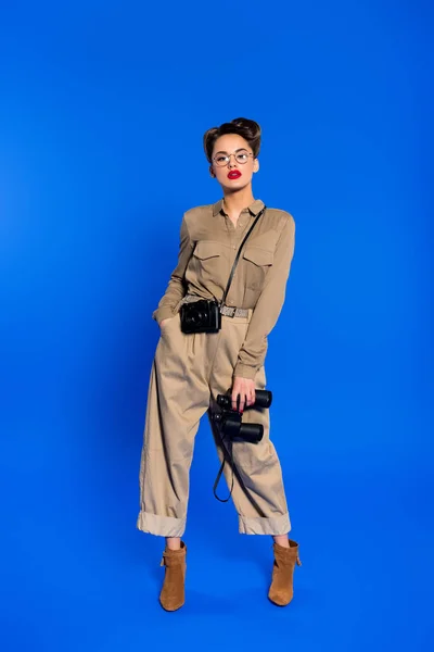 Stylische junge Frau mit Fernglas und Fotokamera isoliert auf blau — Stockfoto