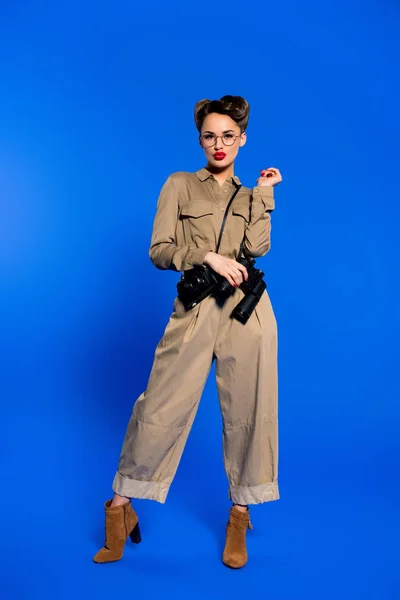 Mujer joven de moda en ropa retro con cámara fotográfica y binoculares aislados en azul - foto de stock