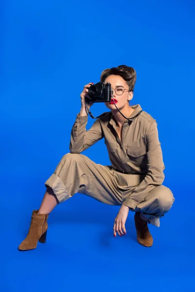 Giovane donna alla moda in abiti retrò con fotocamera isolata su blu — Foto stock