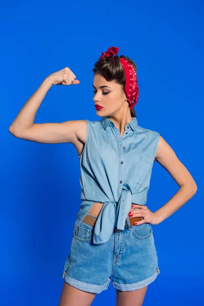 Porträt einer jungen Frau in Retro-Kleidung, die Muskeln isoliert auf blau zeigt — Stockfoto