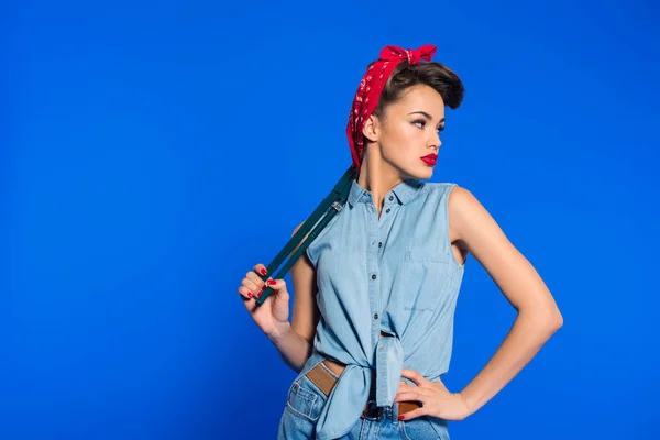 Mujer joven de moda en pin up ropa de estilo con llave inglesa aislada en azul - foto de stock