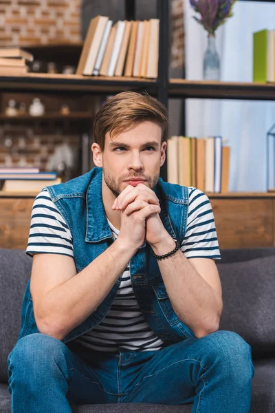 Joven guapo sentado en el sofá y mirando hacia otro lado - foto de stock