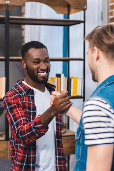 Abgeschnittene Aufnahme von jungen multiethnischen Männern, die sich die Hände reichen und einander anlächeln — Stockfoto