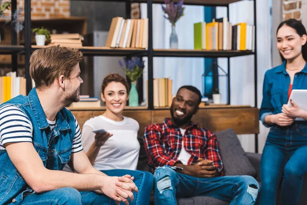 Alegres jóvenes amigos multiétnicos utilizando tableta digital y teléfono inteligente en casa - foto de stock