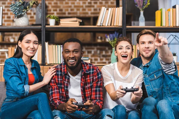 Excited young multiethnic friends playing with joysticks together at home — Stock Photo