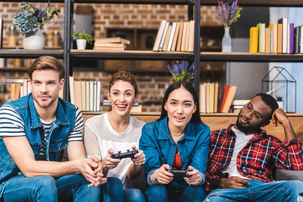 Lächelnde junge multiethnische Freunde, die zu Hause gemeinsam mit Joysticks spielen — Stockfoto