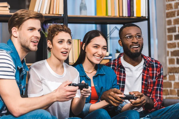 Jóvenes amigos multiétnicos jugando con joysticks juntos en casa - foto de stock