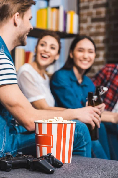 Close-up view of joysticks and popcorn in box and young friends sitting behind — Stock Photo