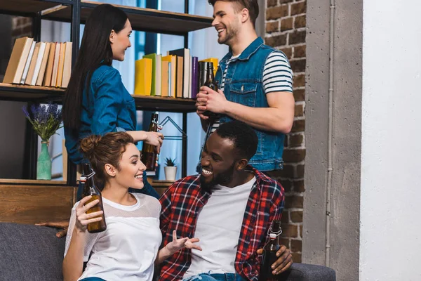 Happy young multiethnic friends drinking beer and talking at home — Stock Photo