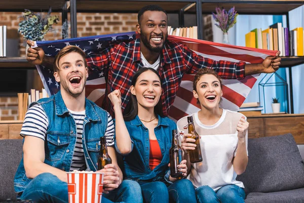 Emotional young multiethnic friends drinking beer and watching tv together — Stock Photo