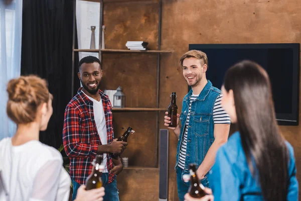 Felizes jovens amigos multiétnicos segurando garrafas de cerveja e olhando uns para os outros — Fotografia de Stock