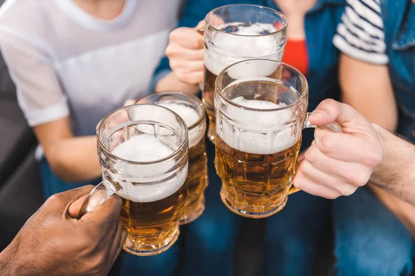Primer plano vista parcial de jóvenes amigos sosteniendo vasos de cerveza en las manos - foto de stock