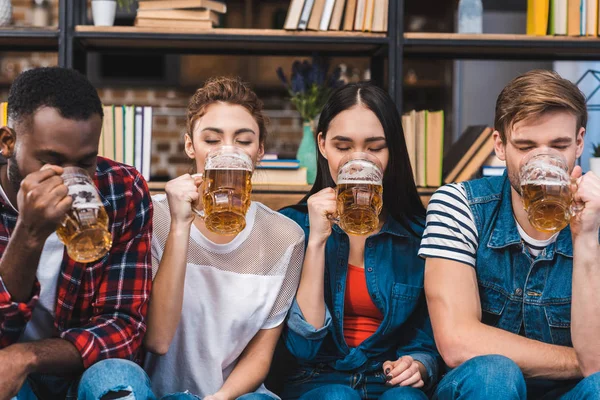 Jóvenes amigos multiétnicos sentados juntos y bebiendo cerveza - foto de stock