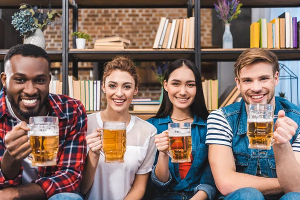 Happy young multiethnic friends holding glasses of beer and smiling at camera — Stock Photo