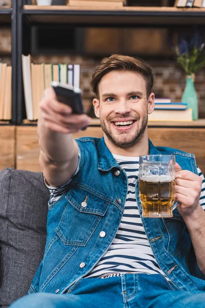 Felice giovane uomo in possesso di un bicchiere di birra e telecomando — Foto stock