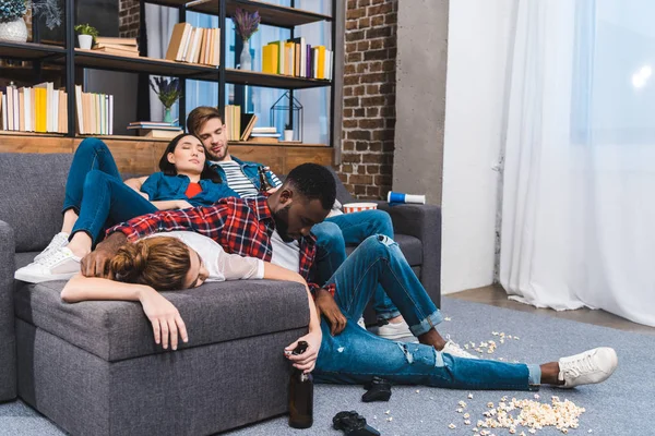 Jeunes amis multiethniques dormant dans une chambre désordonnée avec des bouteilles de maïs soufflé et de bière — Photo de stock