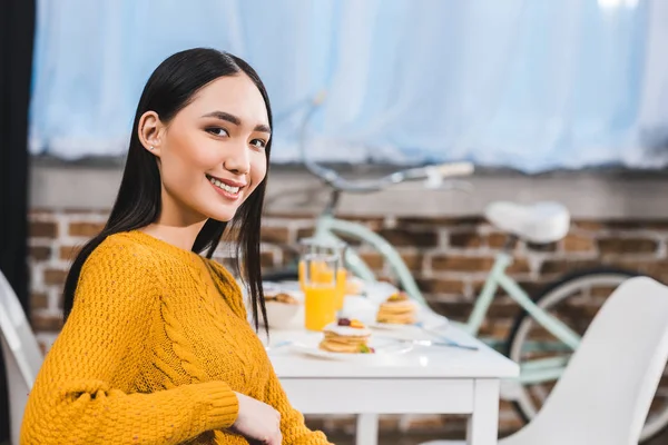 Belle jeune asiatique femme sourire à caméra tandis que assis à la maison — Photo de stock
