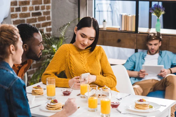 Cropped shot of multiethnic friends looking at asian girl using smartphone at table and young man using digital tablet behind — Stock Photo