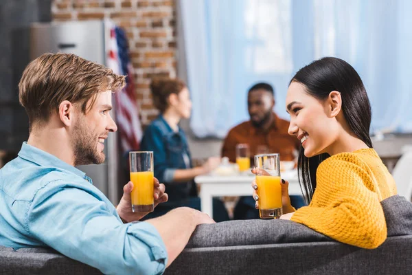 Felice giovane coppia multietnica bere succo e sorridere a casa — Foto stock